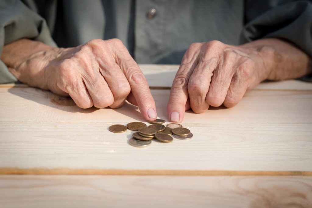 Hände eines älteren Menschen, der nach einem teuren Immobilien Teilverkauf nur noch wenig Geld besitzt